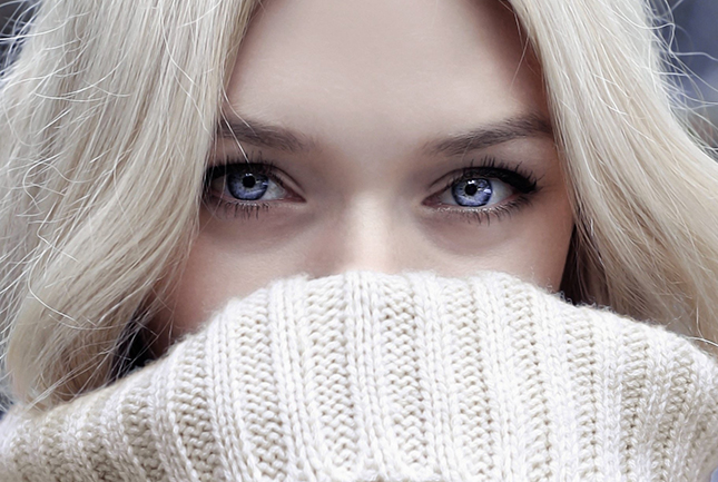 Image of woman snuggling into the neck of her thick cable knit sweater.